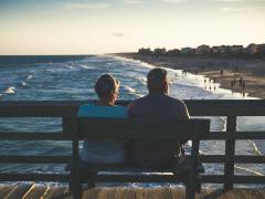 Two older people watching the sunset from a bench