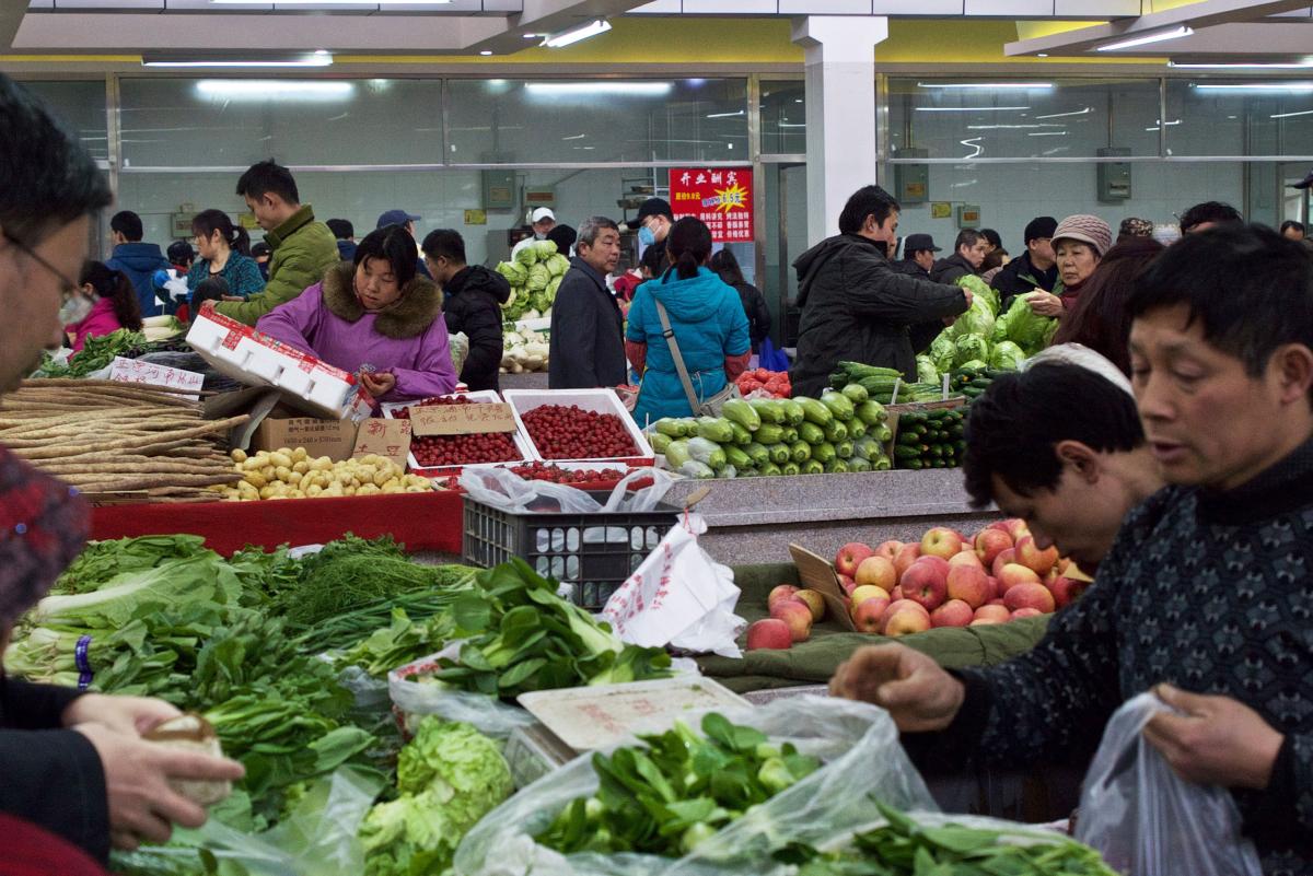 Shoppers in Beijing buying fresh vegetables and fruits in an indoor market.