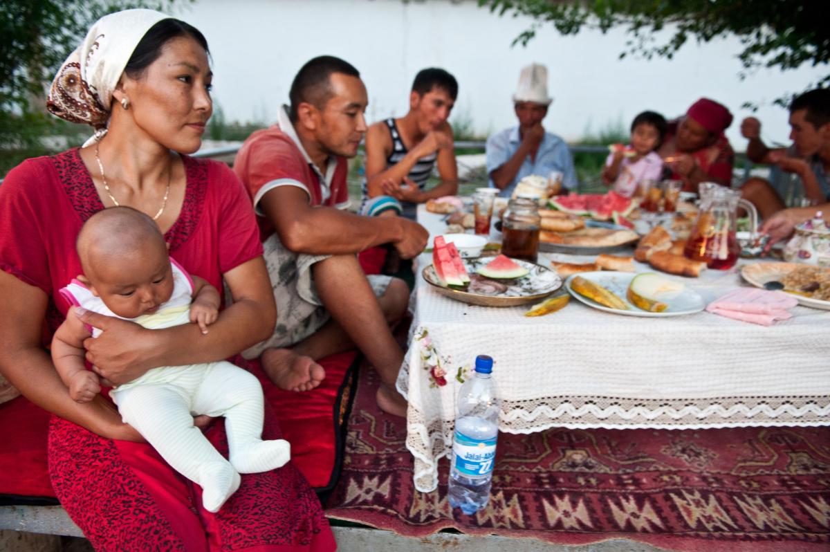 A farming family in Kyrgyzstan takes a break from a day’s work and eats a meal around a table.
