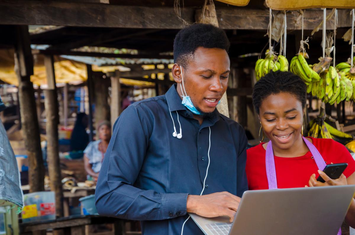 Photo of a man and a woman looking at a laptop in front of a fruit vending stand