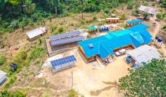 Aerial view of a health clinic in Sierra Leone with blue roof and solar panels in a wooded area.
