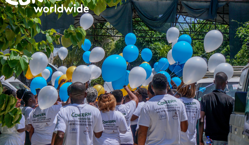 Backs of a group of people wearing CONCERN WORLDWIDE t-shirts and holding balloons 