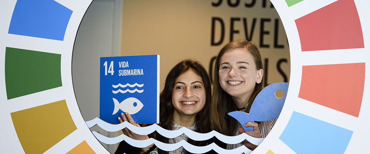 Молодые посетители штаб-квартиры ООН позируют с табличками Целей в области устойчивого развития. Фото ООН/Мануэль Элиас