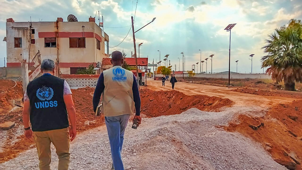 Two men walking on a dirt road with UN branded vests.