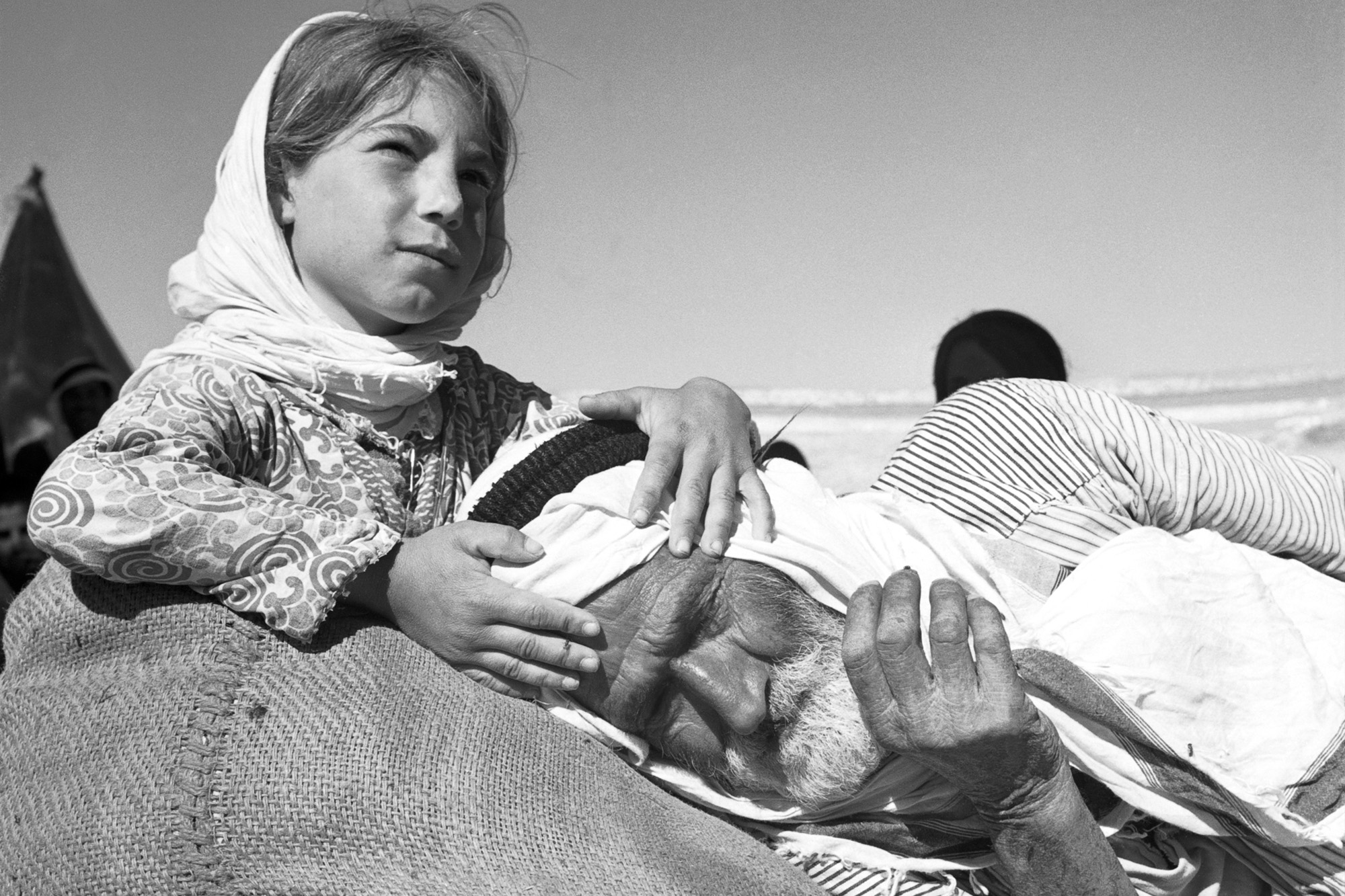 A palestinian girl holding the head of a man resting on a sack.