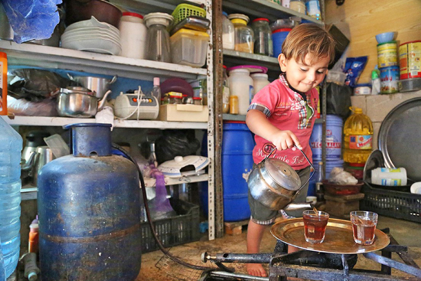 Mohamad, a young boy, pours tea in his family kitchen.