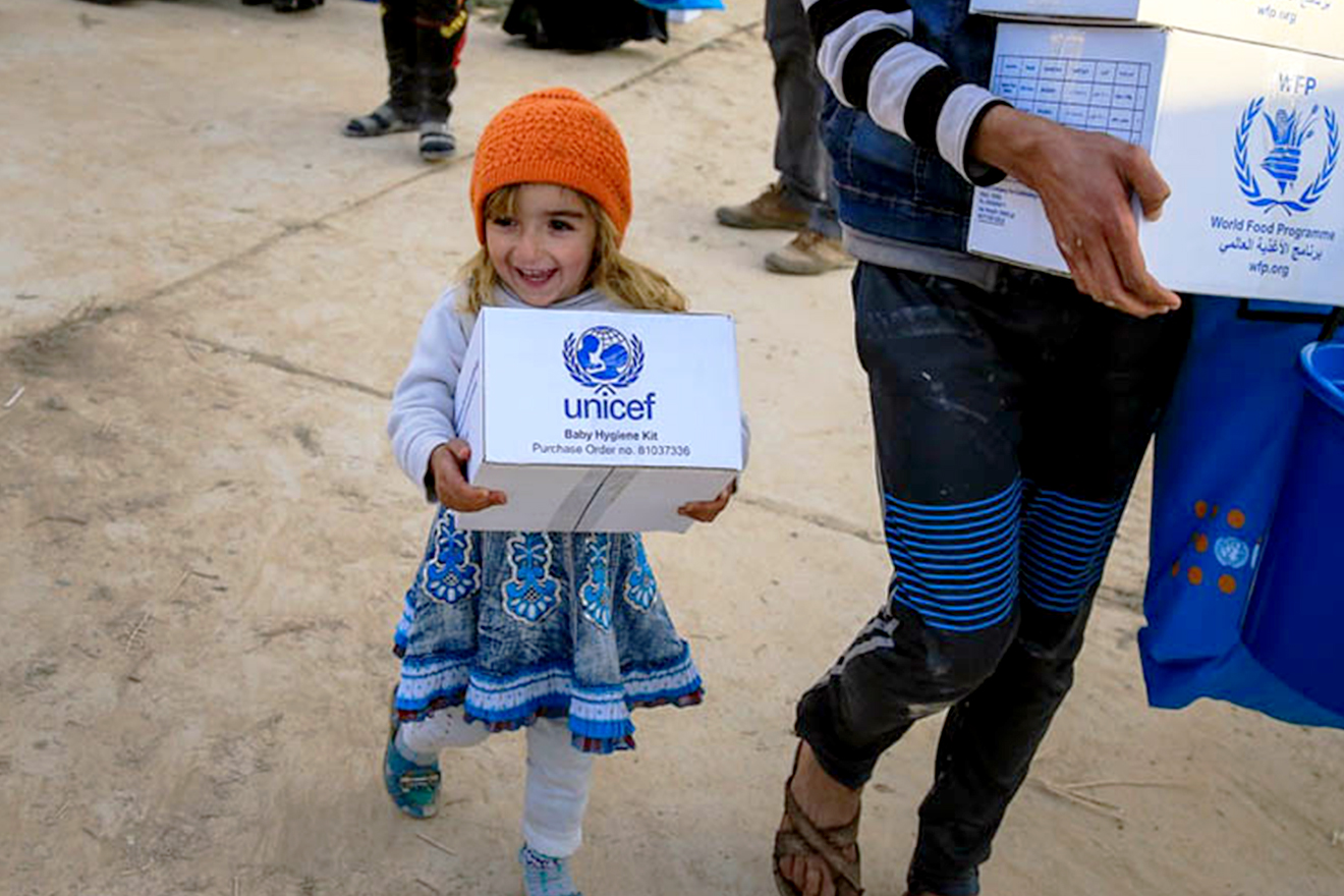 A girl walks away from an aid distribution in Eastern Mosul holding a baby hygiene kit.