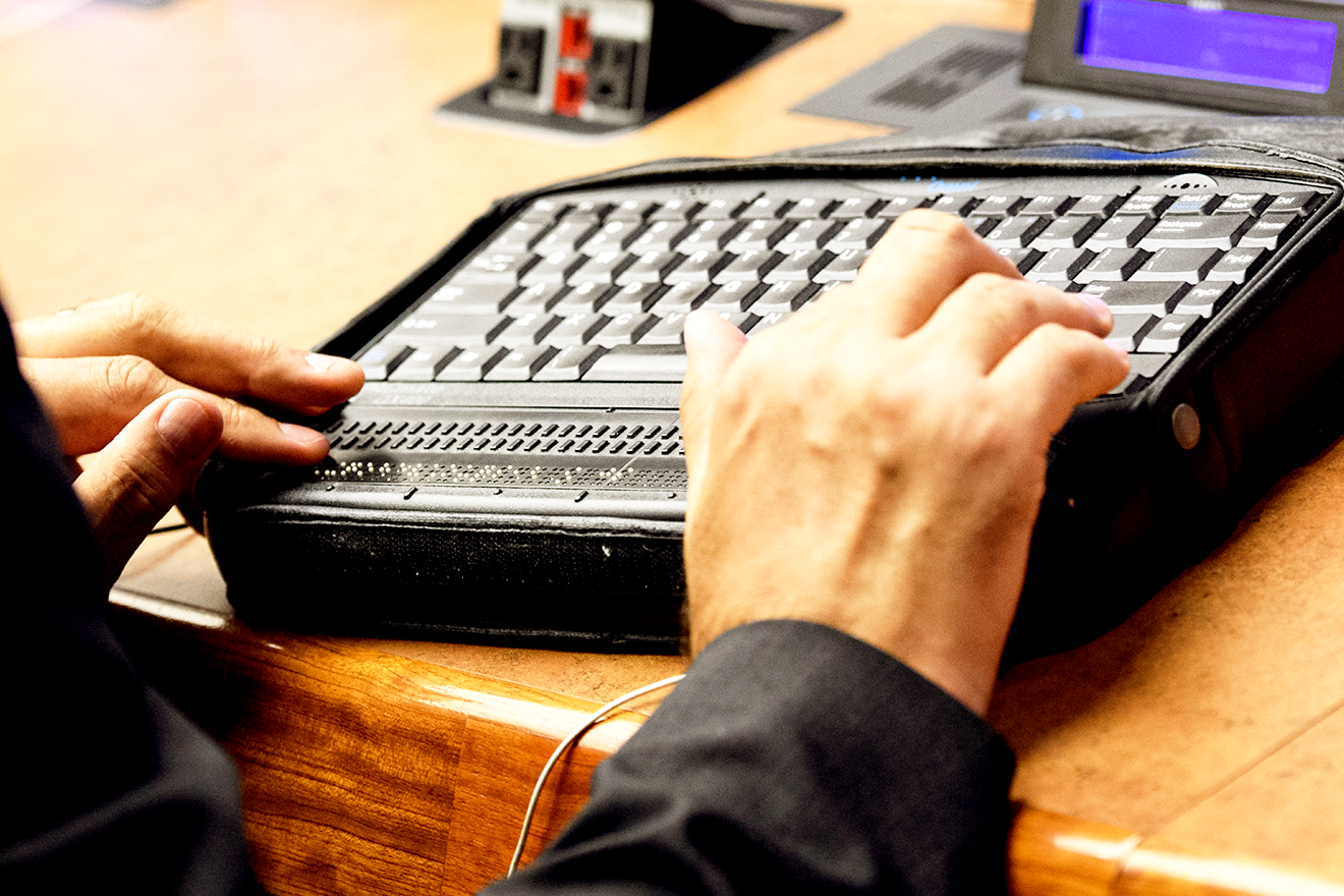 Close up photo of the hands of a person using a braille laptop.