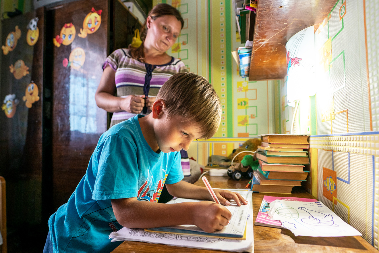Dima practices handwriting at his study corner while his mother looks on.