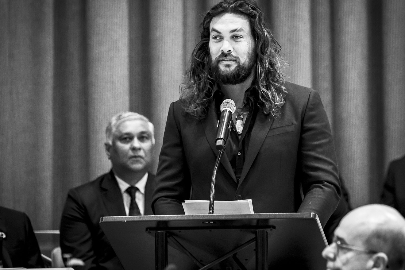 Jason Momoa standing at the podium delivering a speech.