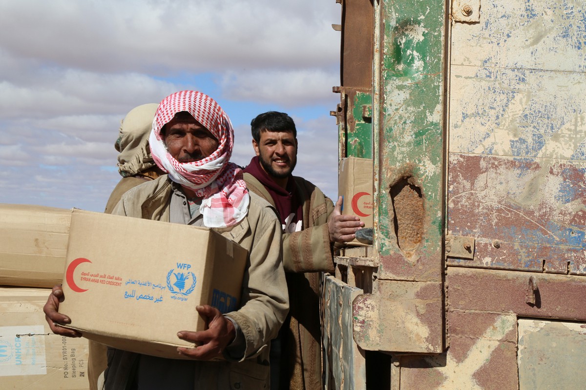 Men collect boxes, which are stamped with the WFP and Syrian Red Cross logos, from the back of a truck.