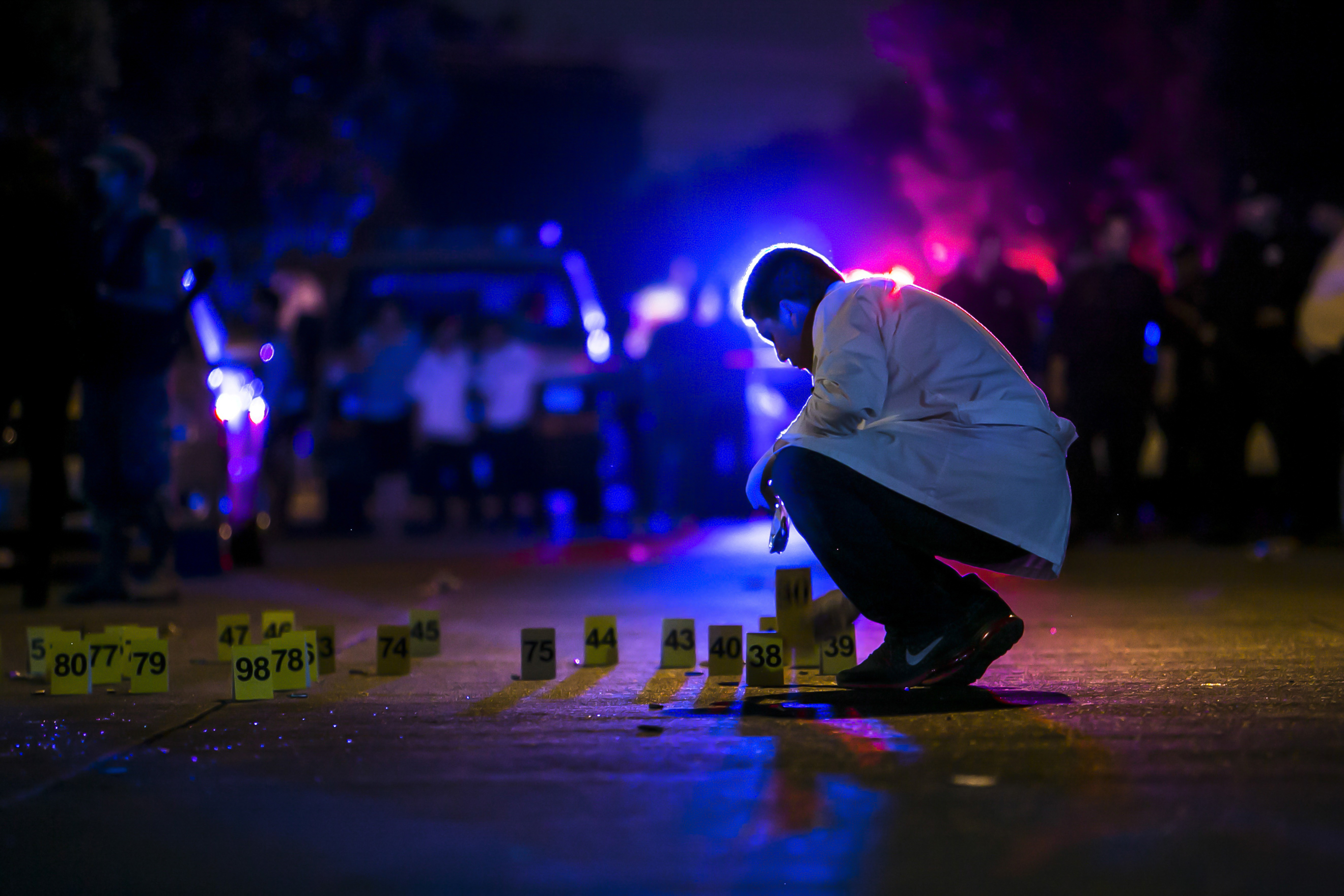 night scene of forensics expert arranging numbered cards on ground