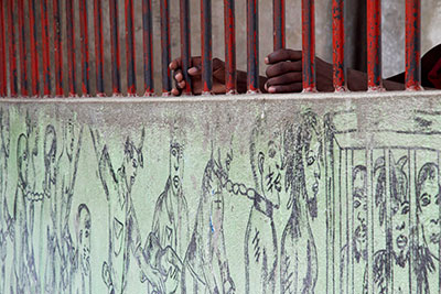 An inmate grasps the bars of an outside wall at the Penitentiary on which a mural of prisoners has been drawn