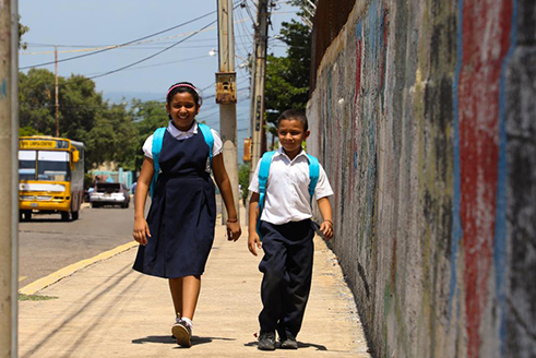 Una niña y un niño venezolanos caminan con sus mochilas de UNICEF.
