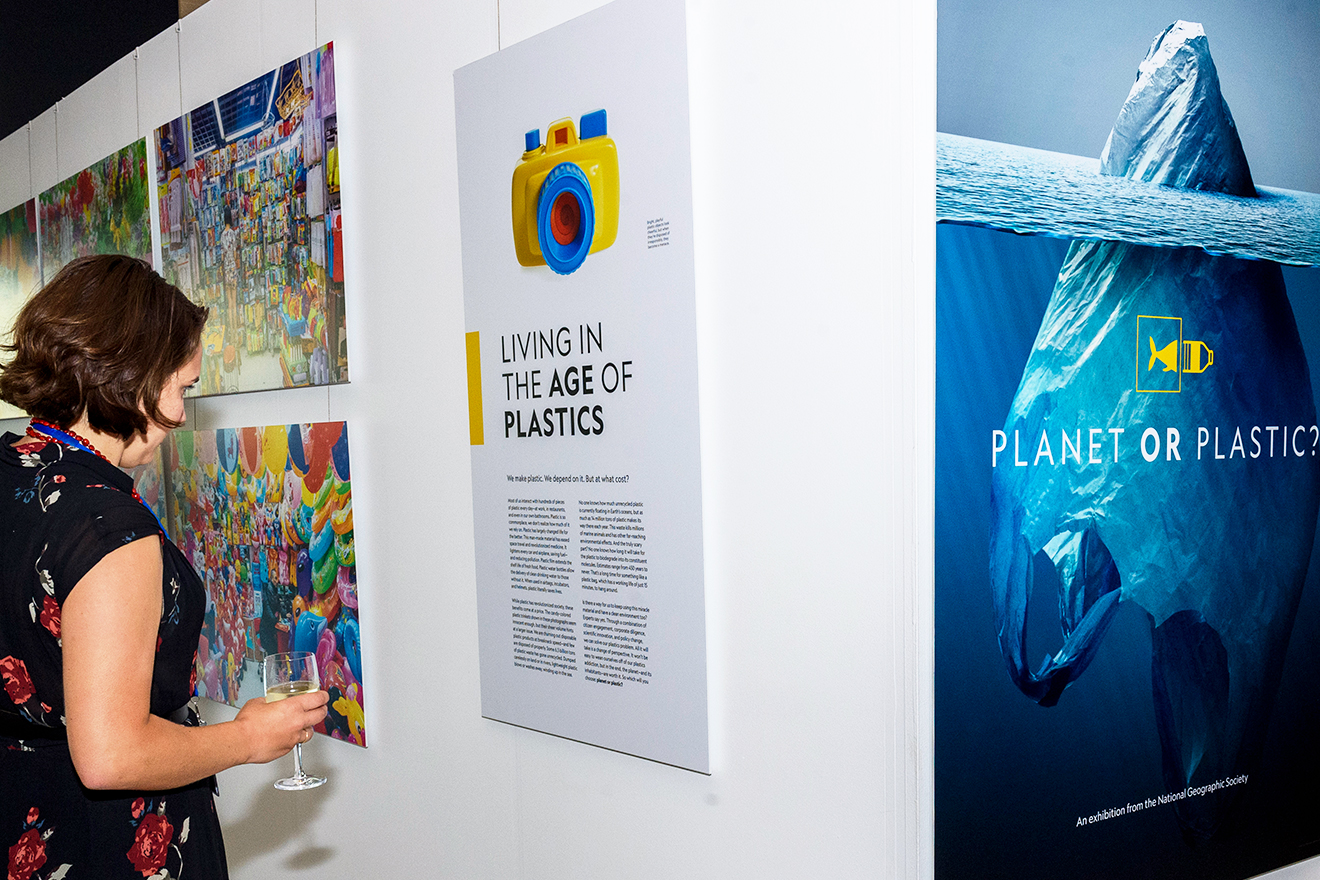 A woman looks at a poster in an opening to an exhibition titled "Planet or Plastic?"