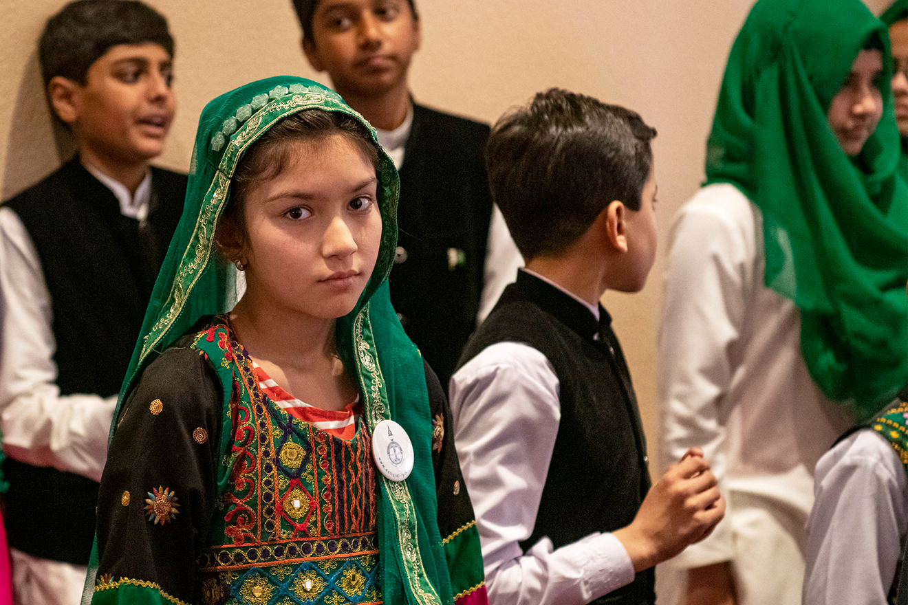 Children lounge about in their national dress and one girl looks pointedly at the camera.