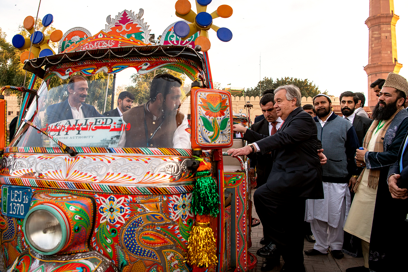 The Secretary-General stands next to a colorful Tuk Tuk and talks to the driver while onlookers stand by.