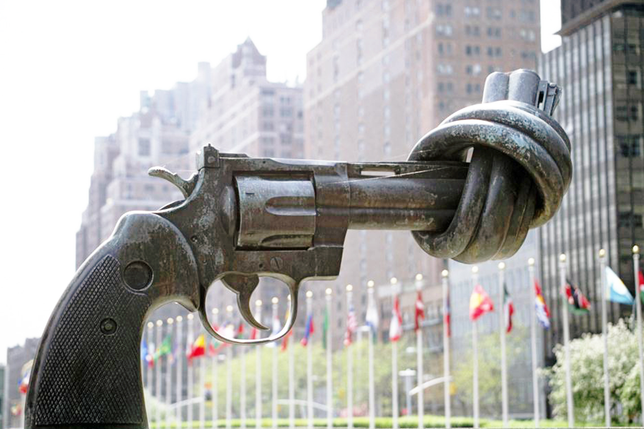 A sculpture of a large scale gun with its nozzle knotted on display at UNHQ with Member States' flags fluttering in the background.