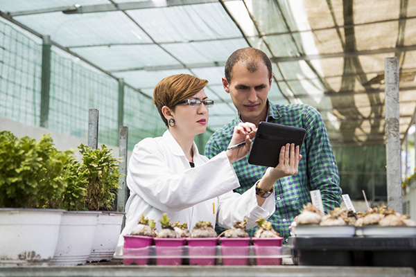 Woman in a lab coat next to a man in a greenhouse