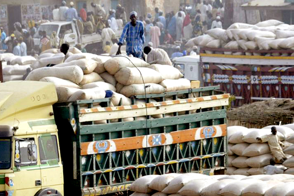 A man sits on top of sacs of food on a truck bed.