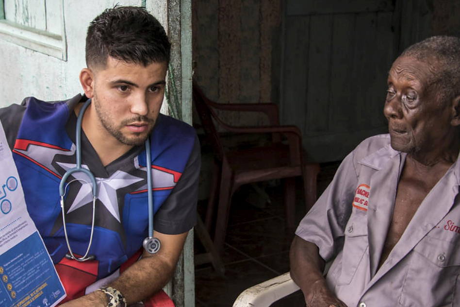 Samuel Suárez shows an elderly Venezuelan a poster of actions to prevent infection.