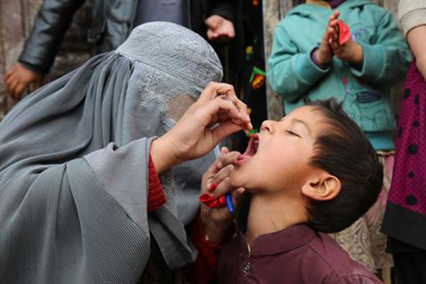 Woman wearing hijab hold a dropper over a boy's open mouth.