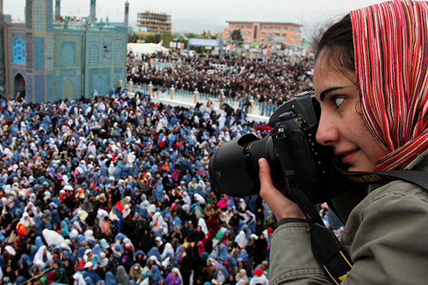 Woman holding camera above a crowd.