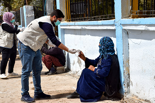 Man handing face mask to woman sitting in the street. 