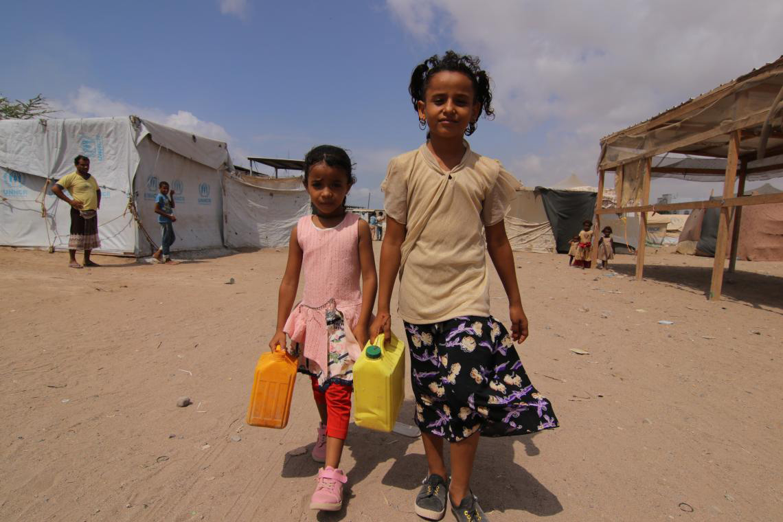 Muna walks with a school friend to the camp’s main water tank to collect clean water for washing and cooking.