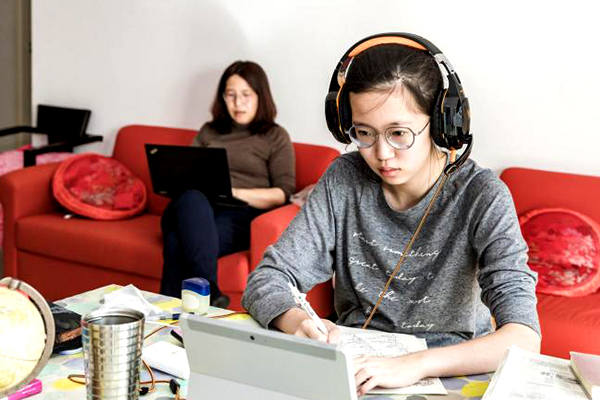 Girl in front of a computer with woman in front of a laptop in the background.