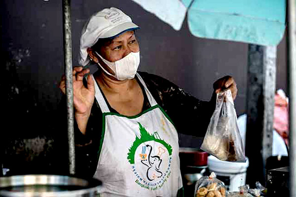 Woman wearing a facemask handing out a plastic bag at a market.