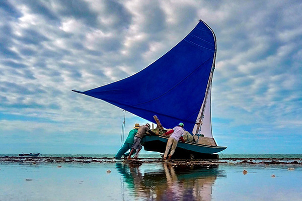 Men pushing a sailboat into the ocean. 