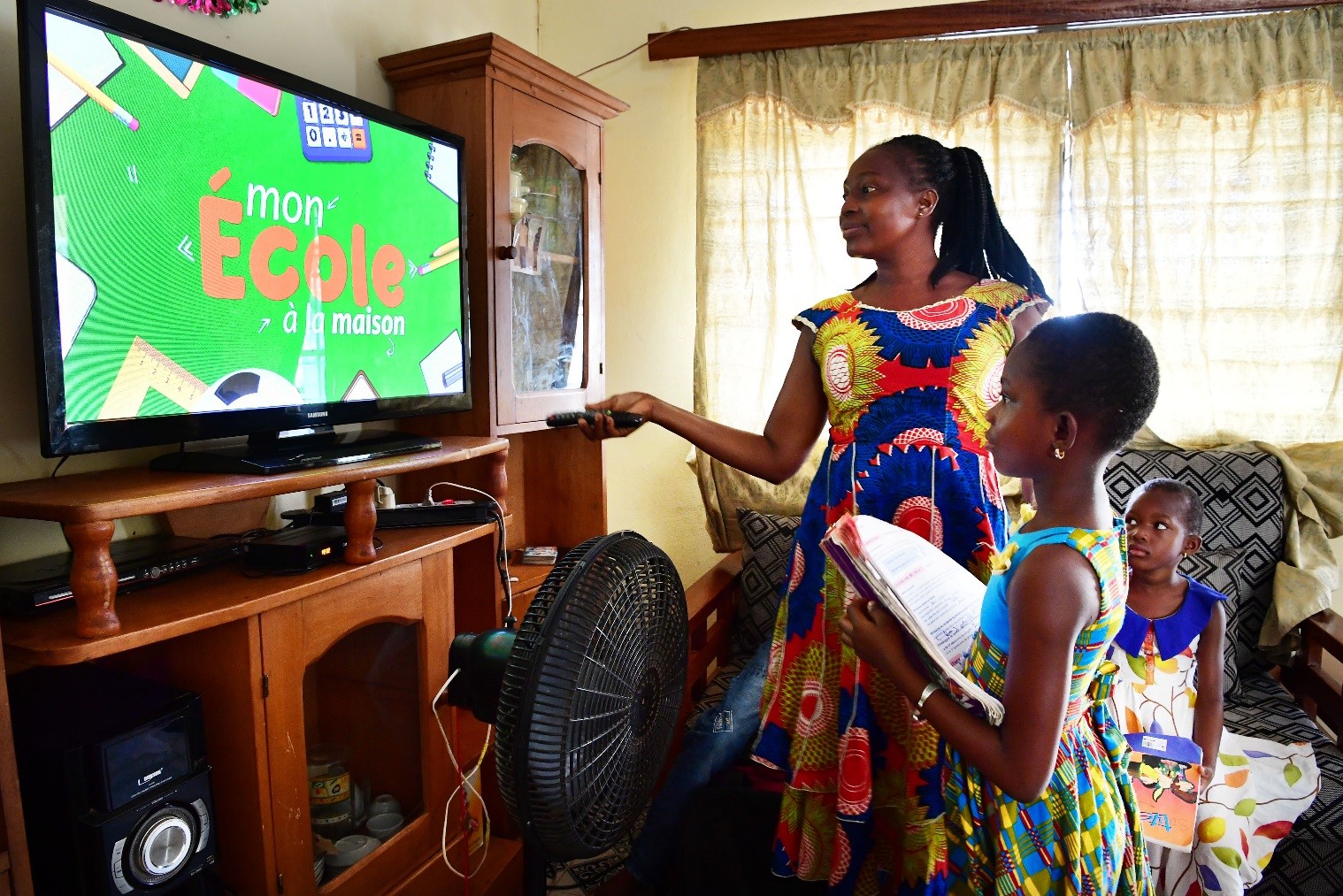 A mother helps her daughter Ange, 8, take classes on television at home 