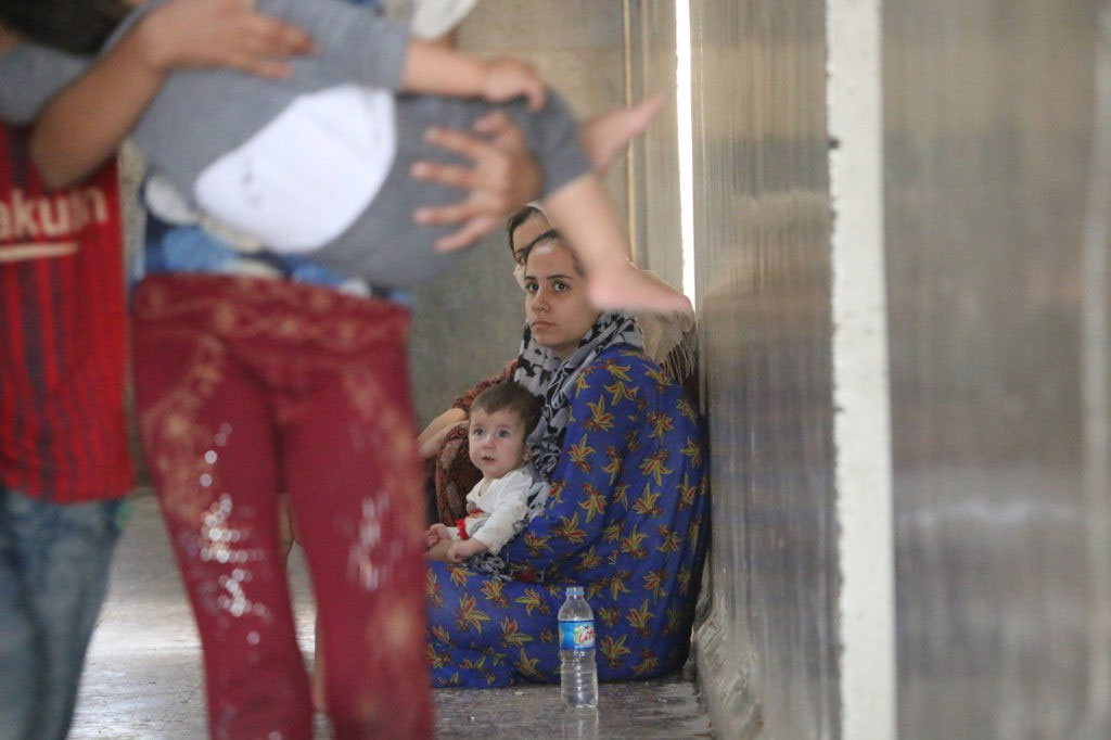 Two women are sitting on the ground, leaning on the wall, with a child in their lap.