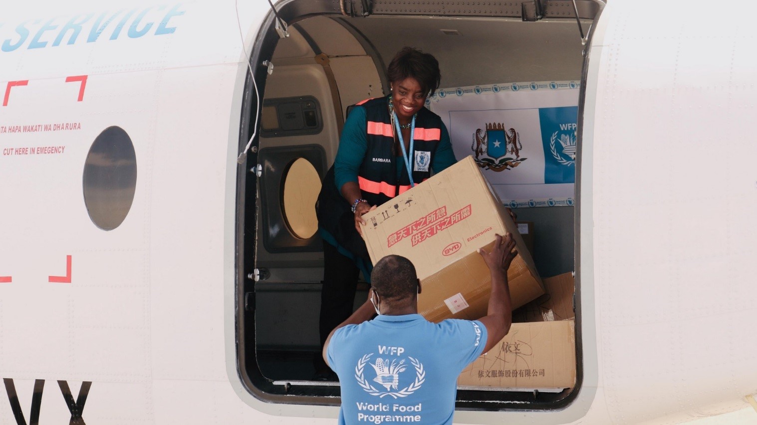 Une femme dans un avion tend un carton à une employée du PAM.