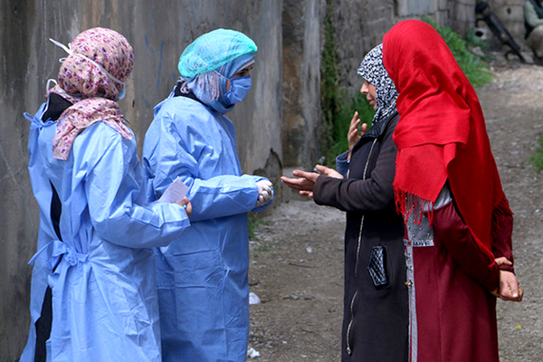 Two women in protective gear speak to two women without face masks.