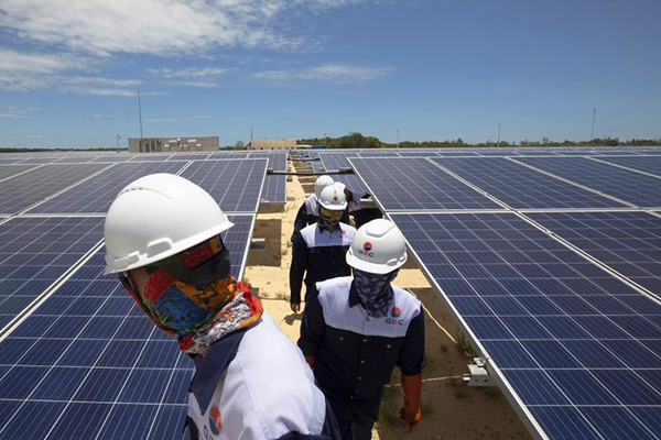 Workers wearing facemasks and helmets among solar panels.