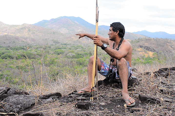 Indigenous man sitting in a rock and pointing a natural area