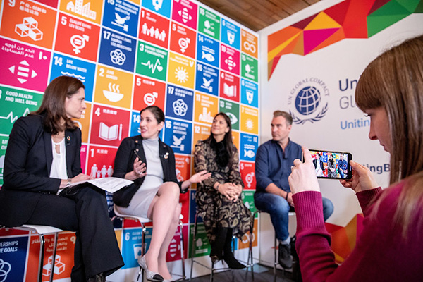 People sitting against a colourful backdrop of the sustainable development goals.