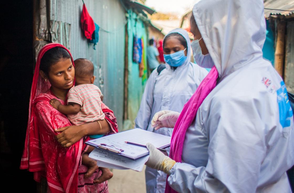 People in protective gear approach a mother with her baby.