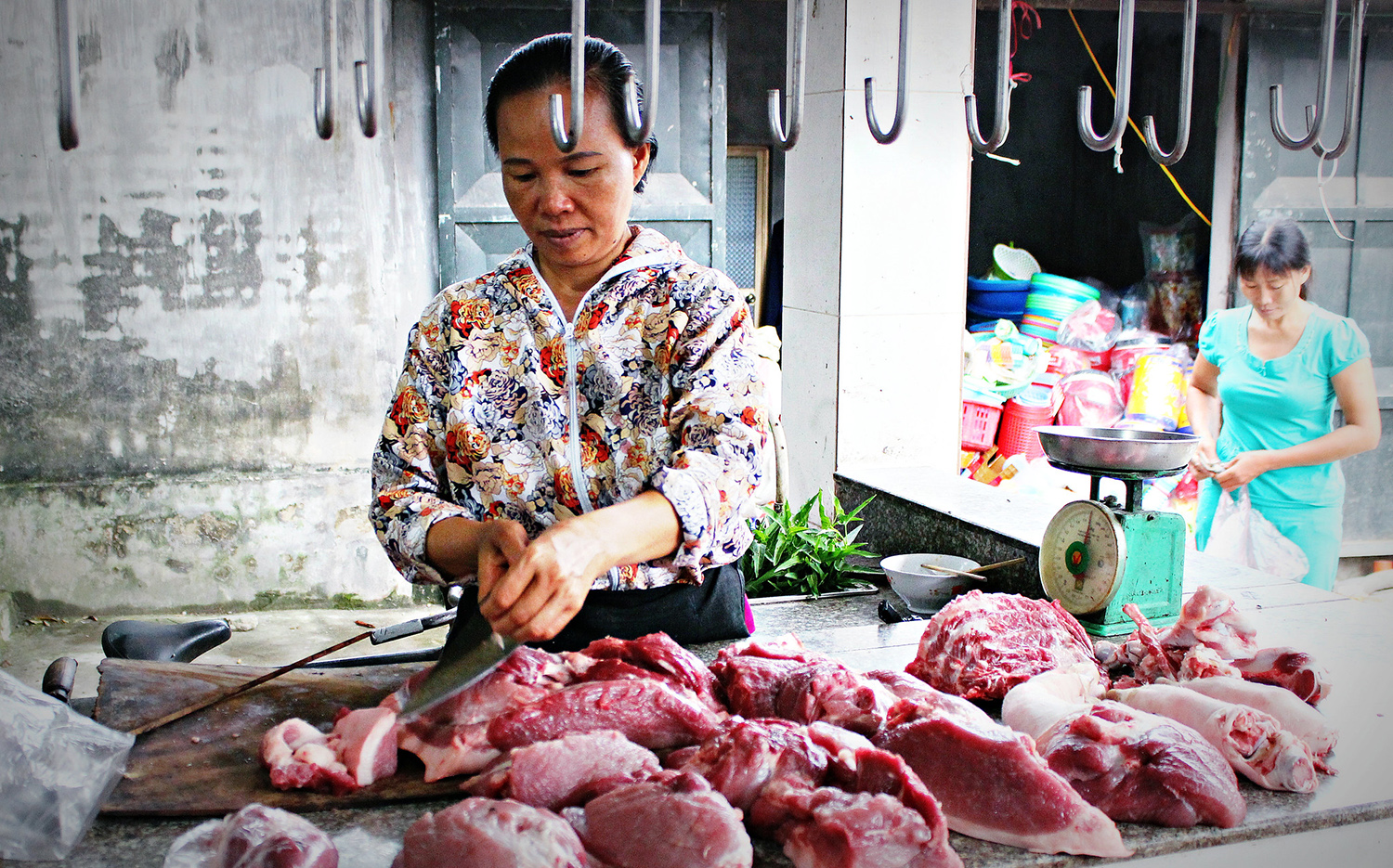 A woman chops meat in an open air market.