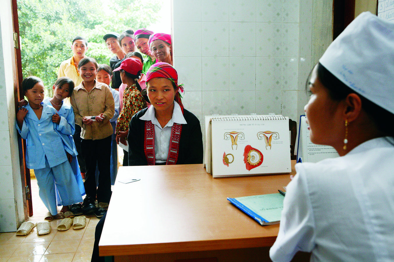 A woman at a health clinic with people looking in from the doorway.