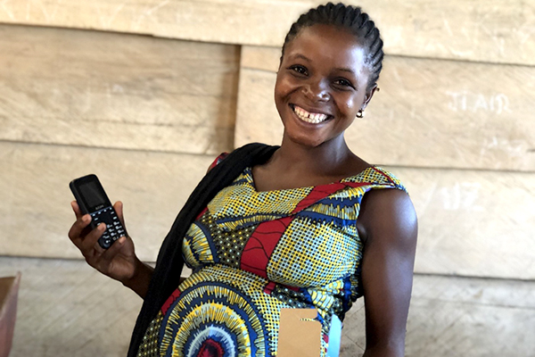 A pregnant woman, holding up a mobile phone smiles. 