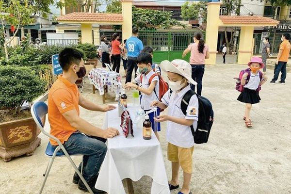 A boy uses hand sanitizer at desks set up in front of a building. 