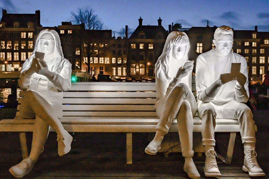 Statue of three kids sitting down looking down at their mobile phones. 