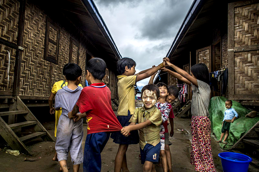 Children play in a line walking under an arch formed by two children holding hands.