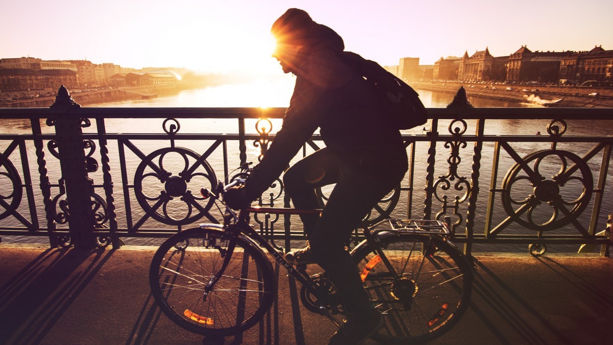 man riding a bicycle with the sun setting in the background