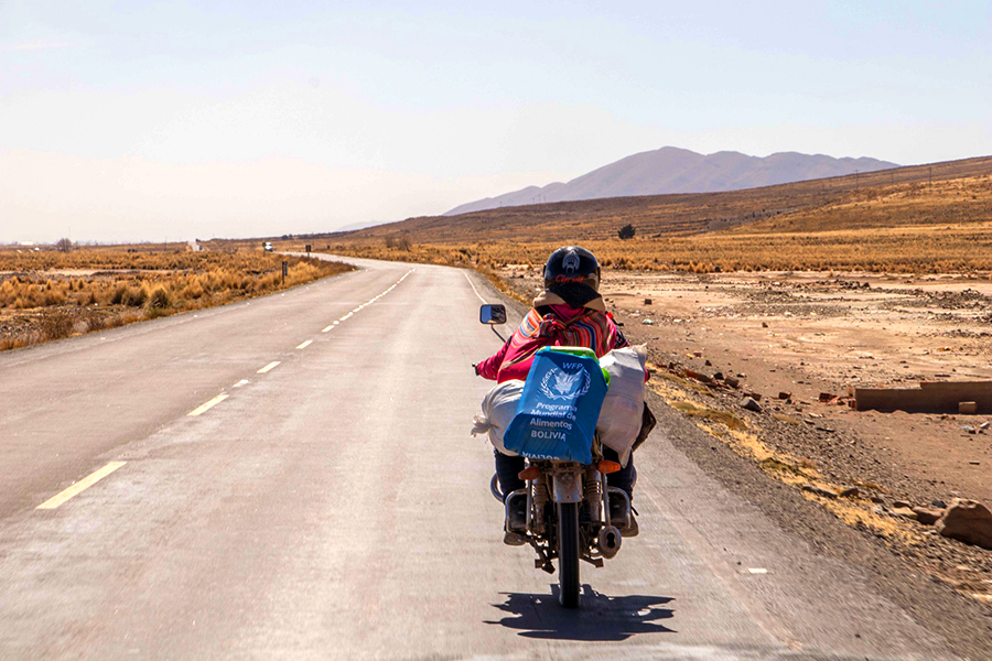 A woman riding a motorcycle carrying a WFP bag.