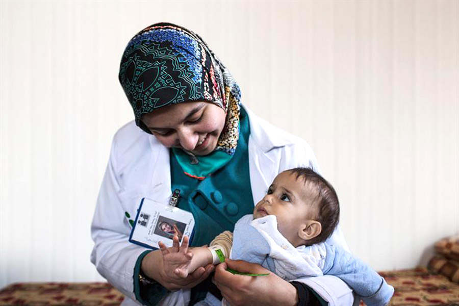 A woman in a lab coat measures a baby’s arm.