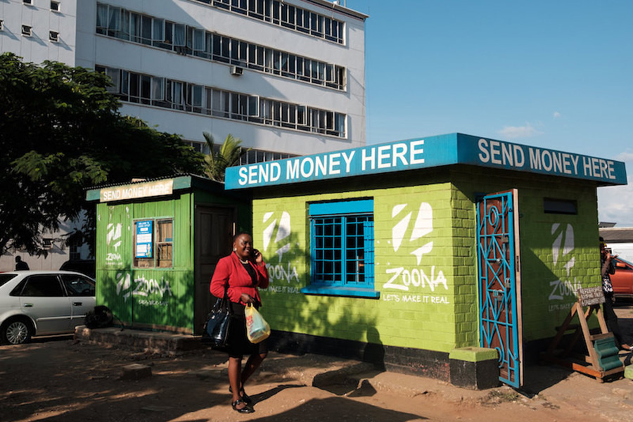 Woman walking by a store with a sign that reads “Send money here”.